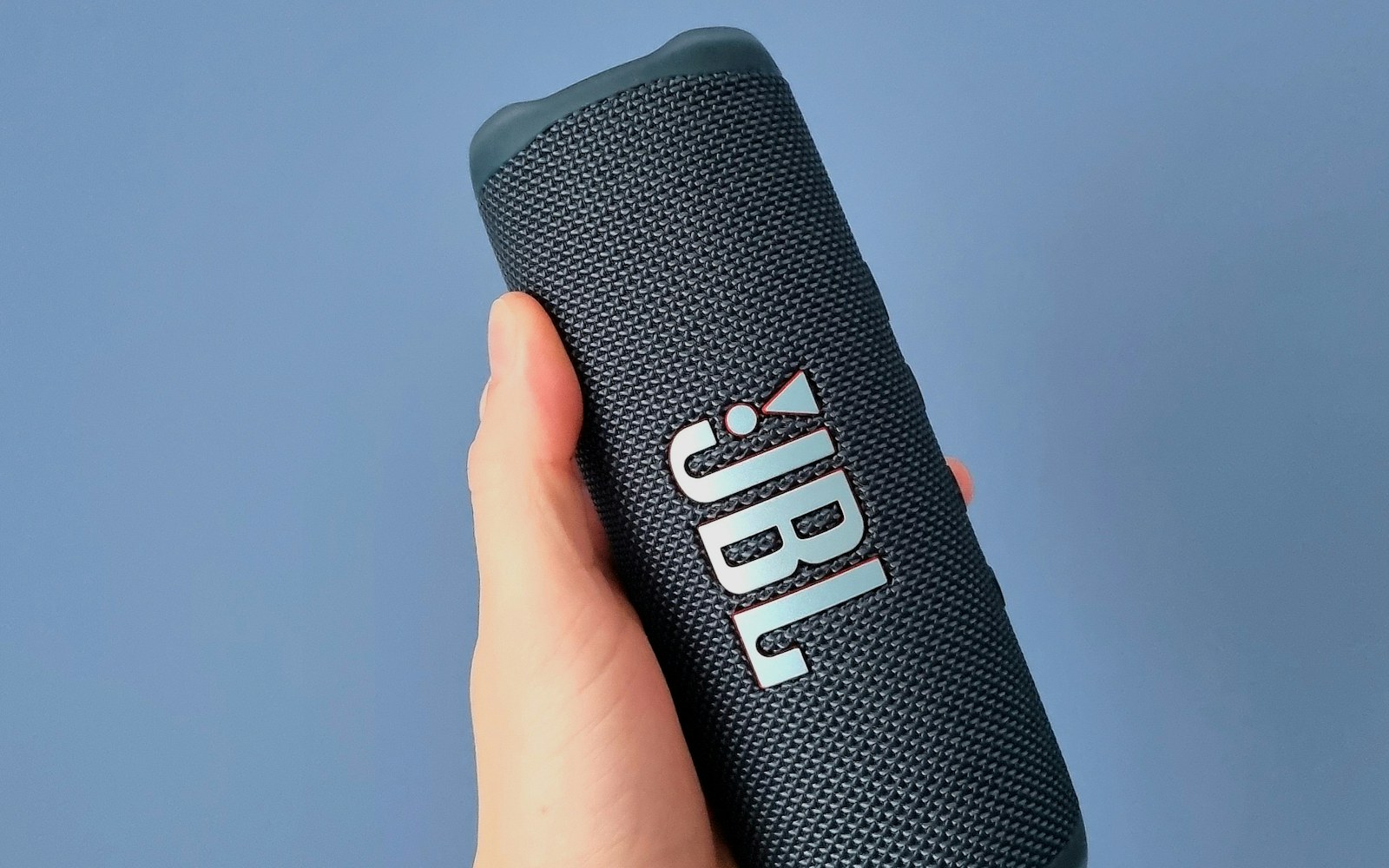 Portable Bluetooth speaker held against a blue background